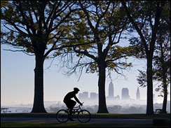 Biker riding in park with trees and Cleveland skyline.
